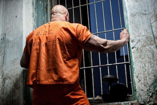 Inmate in orange jumpsuit looking out prison bar window