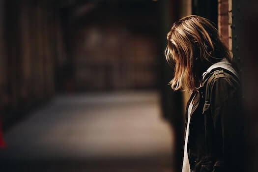 Woman in Jacket and Hoodie Stands Against a Steel Beam in Empty Warehouse Looking Down