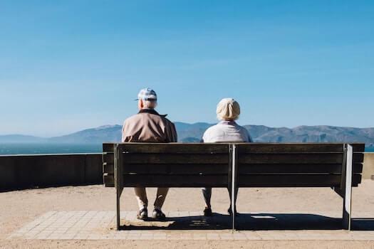 Two Older Adults Sitting on a Bench Looking at a Mountainous Landscape