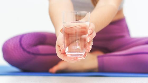 woman with a glass of water on a yoga mat