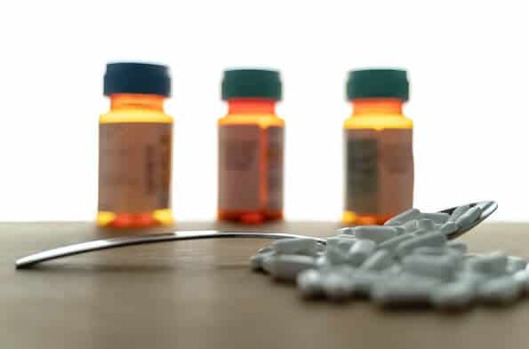 Three pill bottles behind a spoon and pills on table