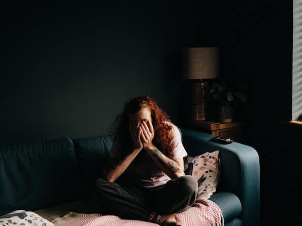 Man Sits on Couch Alone with Head in Hands in Dark Room