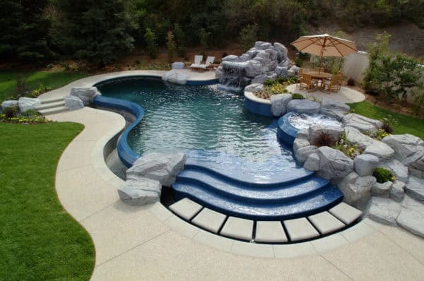 go for a custom-shaped pool in a classic backyard design with stamped concrete deck and stunning water features