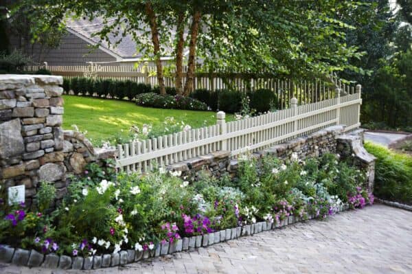 try a short picket fence on a retaining wall made of moss rock stones for privacy without blocking the view