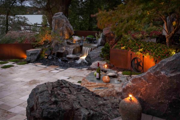 combine corten steel retaining wall and stone sculptures with warm lighting for a dark yet sophisticated landscape