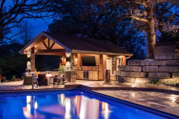 large craftsman pool house with a cozy bathroom to complete this charming stone backyard