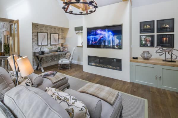 opulent living and study inspired by cottage aesthetics uses dark wood floors, linear fireplace, and large tv above