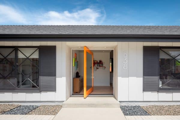 this swiveling orange front door is a centerpiece in this contemporary white home with black window shutters