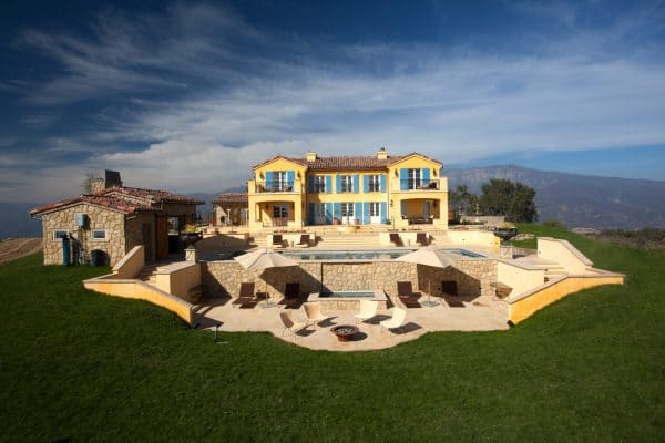 a large, french inspired country yellow house with blue shutters and stucco siding