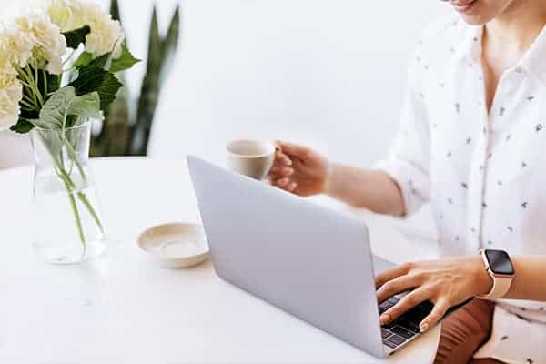 Freelancer on laptop, typing with one hand and a coffee in the other.