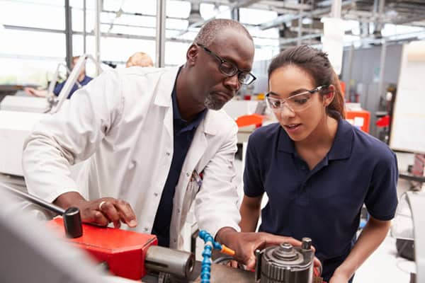 a man showing a young apprentice how to work a piece of machinery