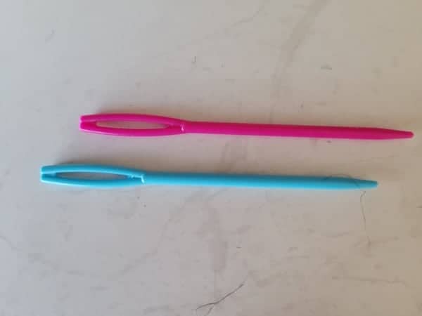 A pink and aqua kids sewing needle with a large eye for easy threading. 