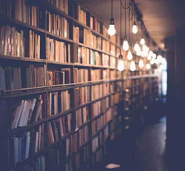 Long library shelf of books behind low hanging bulbs