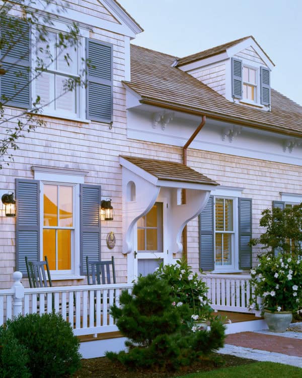 go for a charming exterior featuring a roof over door entry, gray clapboards, and white fence