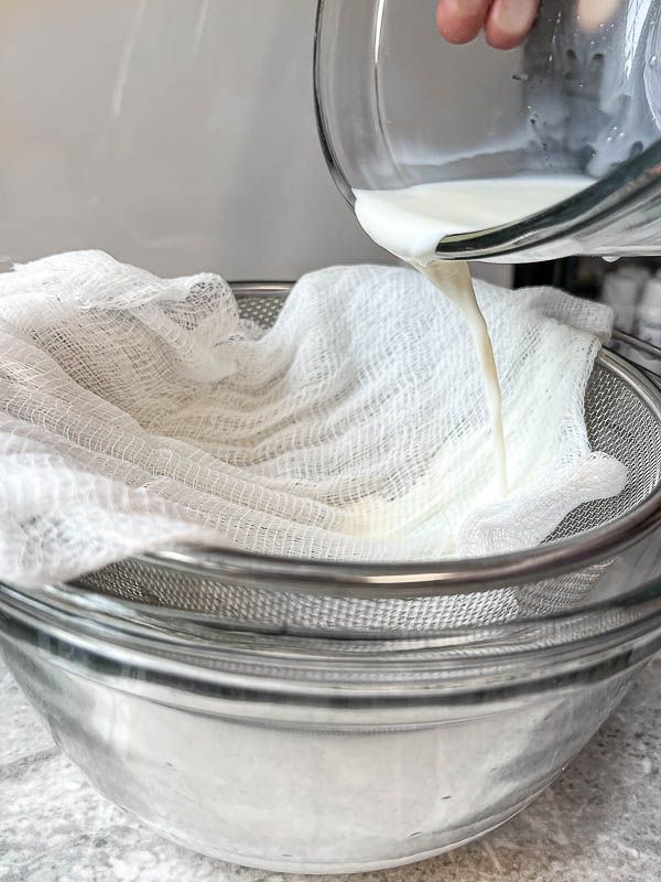 straining goat milk from a glass bowl into cheesecloth