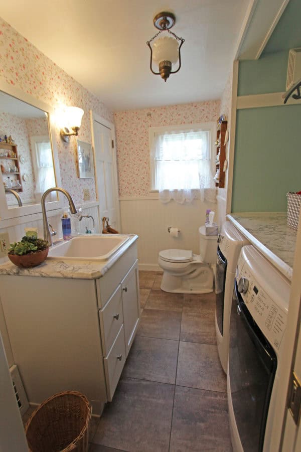 farmhouse bathroom and laundry combo has built-in countertop and floral wallpaper