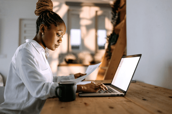 A side view of a contractor typing on their laptop with their right hand, whilst holding a piece of paper in their left hand