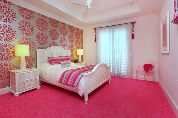 a pink floor area and a wall with pink patterns behind a white wooden bed