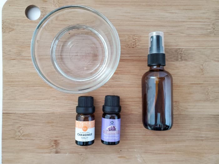 Bowl of water, spray bottle and essential oil bottles on a wood board.
