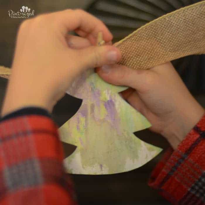 childs hands pinning a paper tree onto burlap ribbon