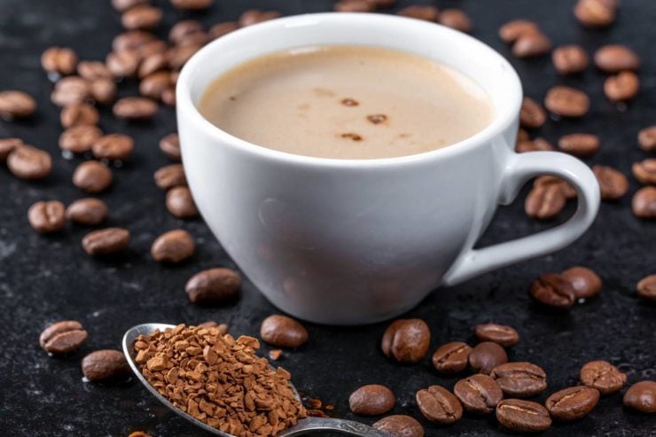 a cup of coffee on a table with sprinkled coffee beans