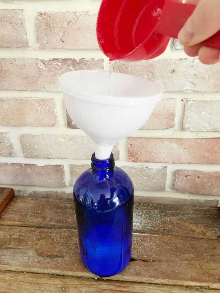 blue bottle with funnel in it pouring in liquid for homemade OxiClean