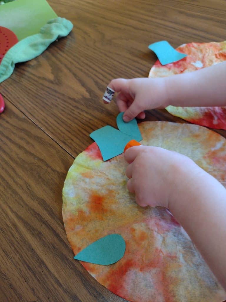 Picture of a preschooler gluing a leaf onto her pumpkin jack o'lantern craft