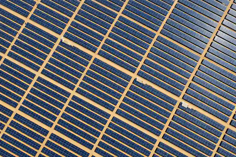 Vista aérea de un parque fotovoltaico español de gran escala con miles de paneles solares azules en alineación geométrica, capturada desde 150 metros de altura en luz cenital
