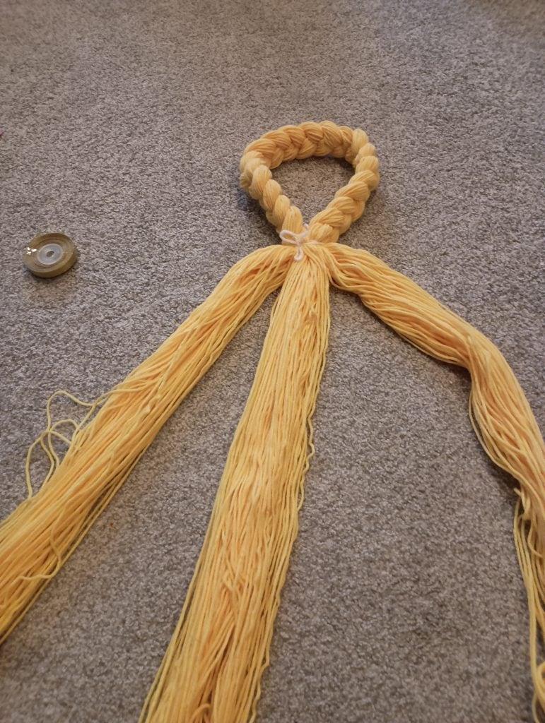 Picture of braided yellow yarn tied in a loop with the remaining loose yarn separated into three sections