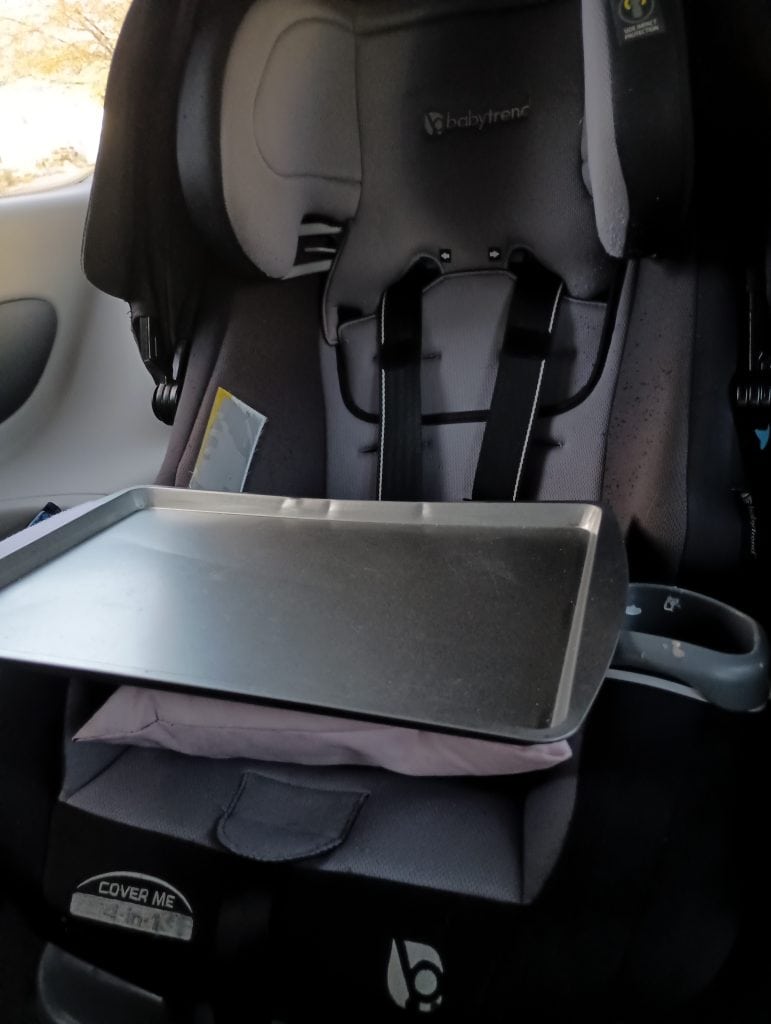 Picture of a DIY car seat tray made of a cookie sheet and a pink pillow attached to a car seat