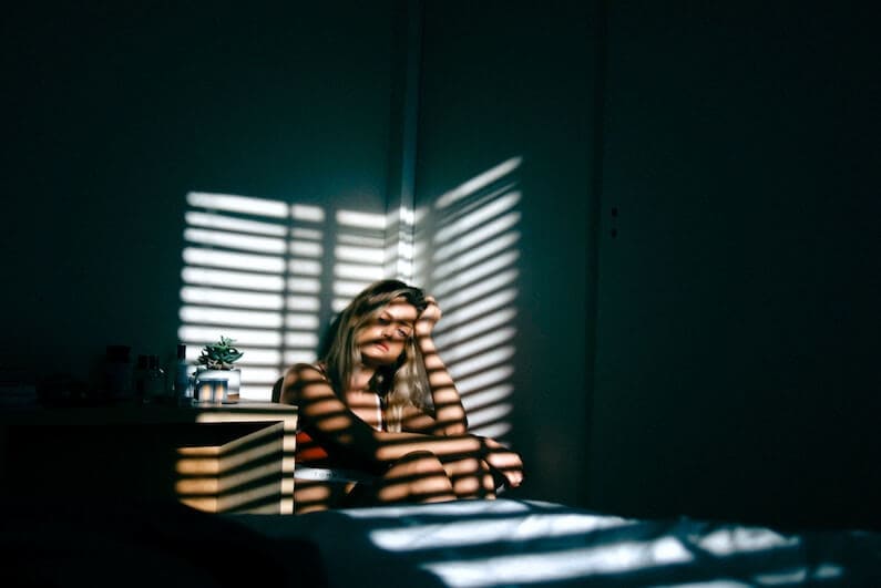 girl suffering from opioid abuse sitting in dark room with head between knees