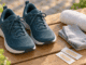 Dunkle Sportschuhe, graue Socken, Handtuch und zwei Pflaster auf einer Holzbank; KI-generiertes Symbolbild.