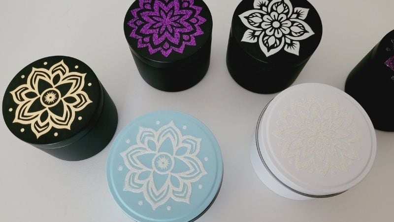 Finished HTV Mandala designs on the candle tins. Shown are the designs created with HTVRont purple glitter HTV, white glitter HTV and the Cricut brand gold foil for the ScanNCut Vinyl Cutting Tutorial