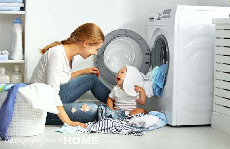 mom with a baby engaged in laundry fold clothes into the washing machine