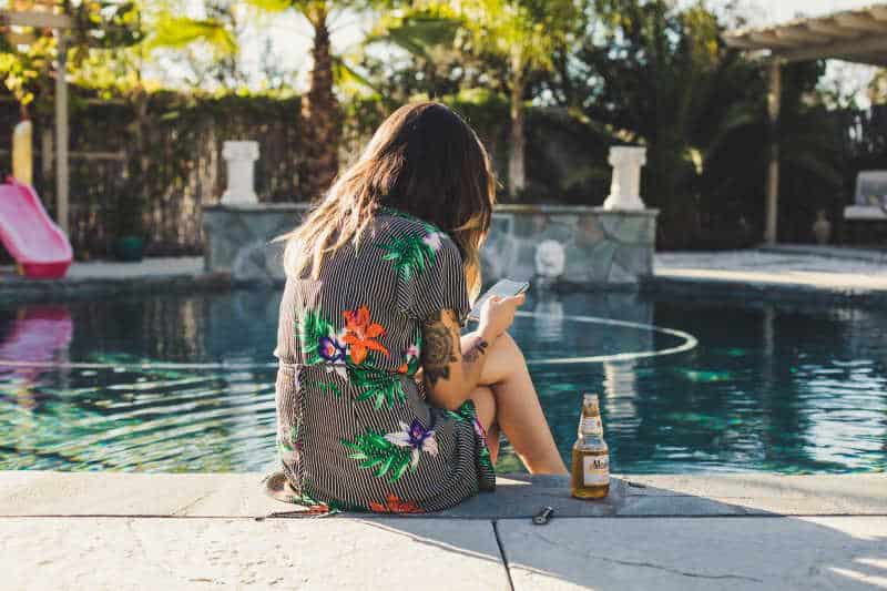 A woman sitting by a pool reading on her phone. Photo by Kvnga on Unsplash