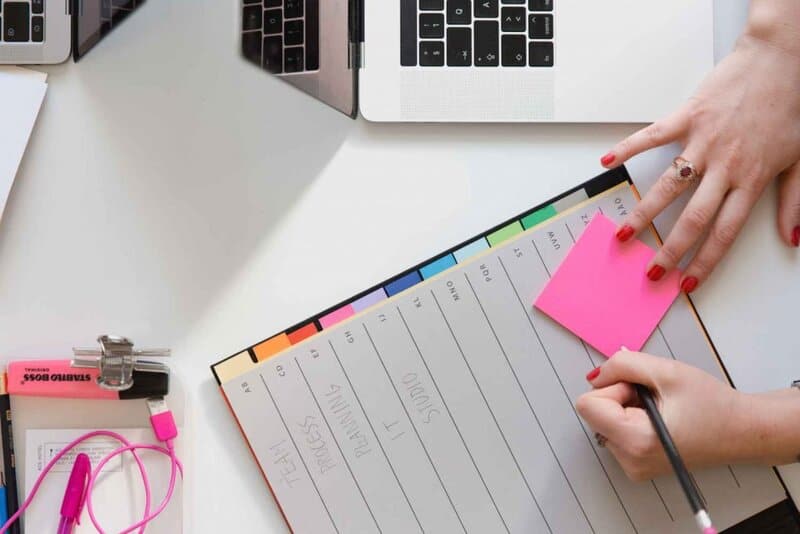 Photo of someone writing on a sticky note with a planner. Photo by Marten Bjork.