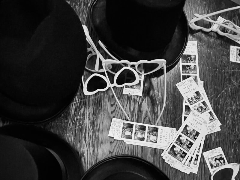Kapelusze, okulary w kształcie serc i stos wydruków 5×15 cm z fotobudki na drewnianej podłodze