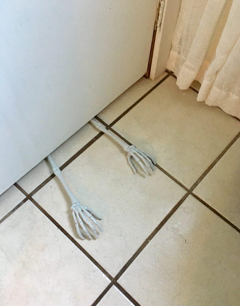 skeleton arms poke out from under a bathroom closet door.