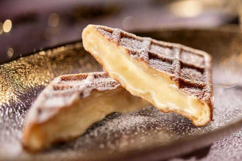 Warm custard-filled waffle cone dessert with powdered sugar on a textured surface.