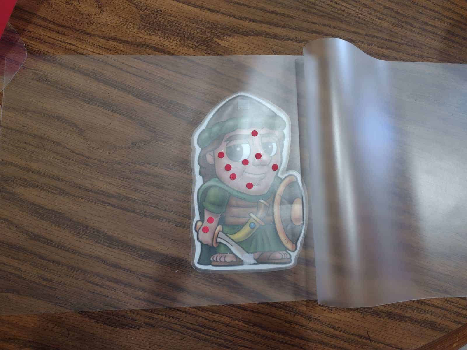 Picture of red dots on an open laminating pouch on a picture of Naaman