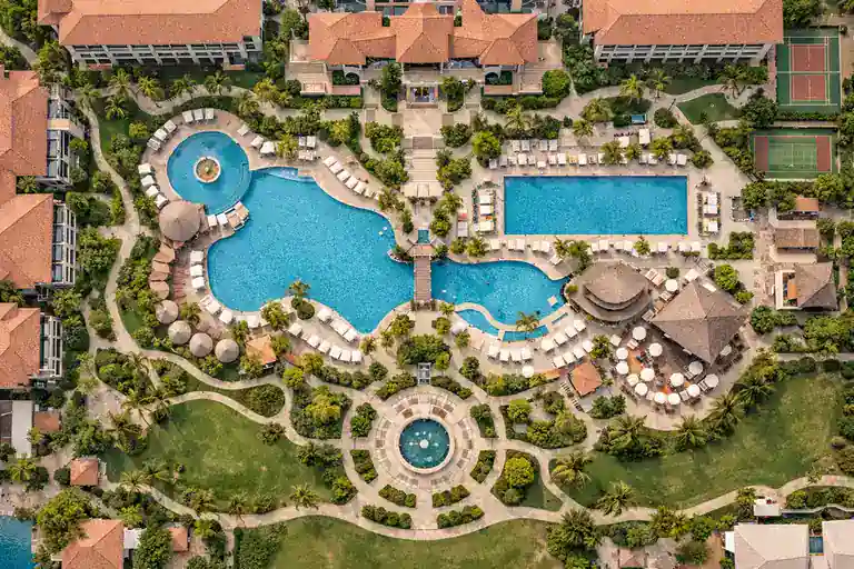 Vista cenital aérea de resort hotelero con piscina y jardines en luz suave