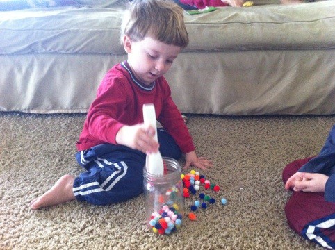 Preschool Child practices motor skills with pom poms.