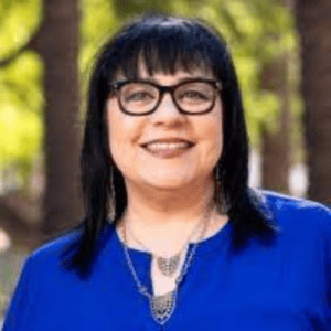 A woman with long dark hair wearing glasses and a blue blouse.