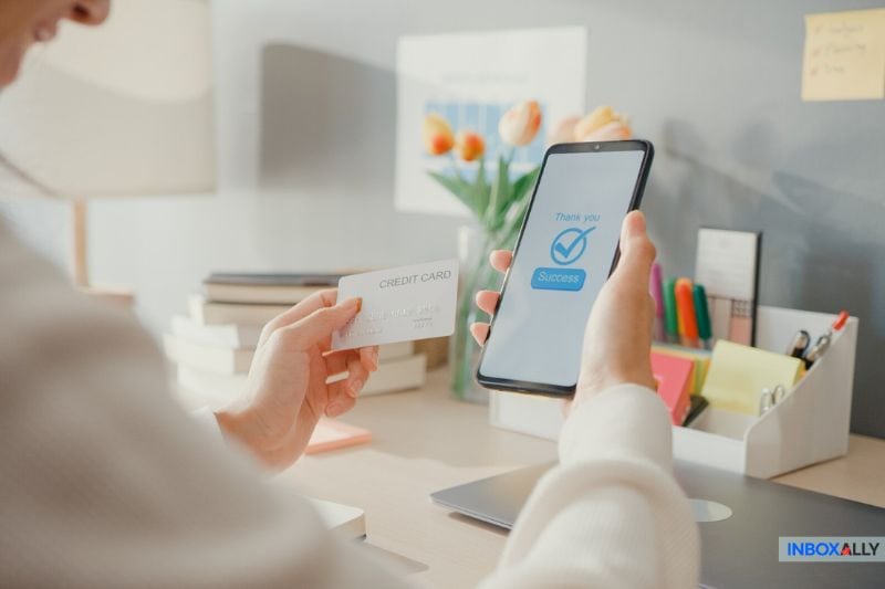 Uma pessoa sorri segurando um cartão de crédito e um smartphone que mostra uma mensagem de 