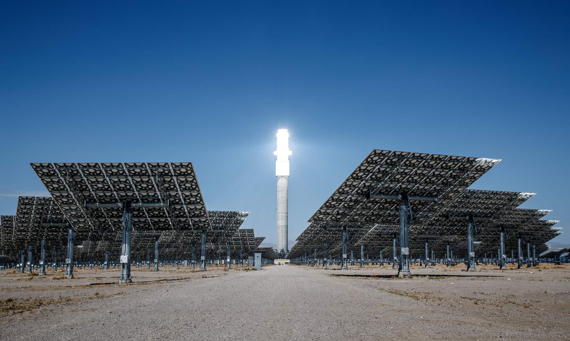 Desert solar thermal plant with hundreds of heliostat mirrors surrounding a tall central receiver tower.