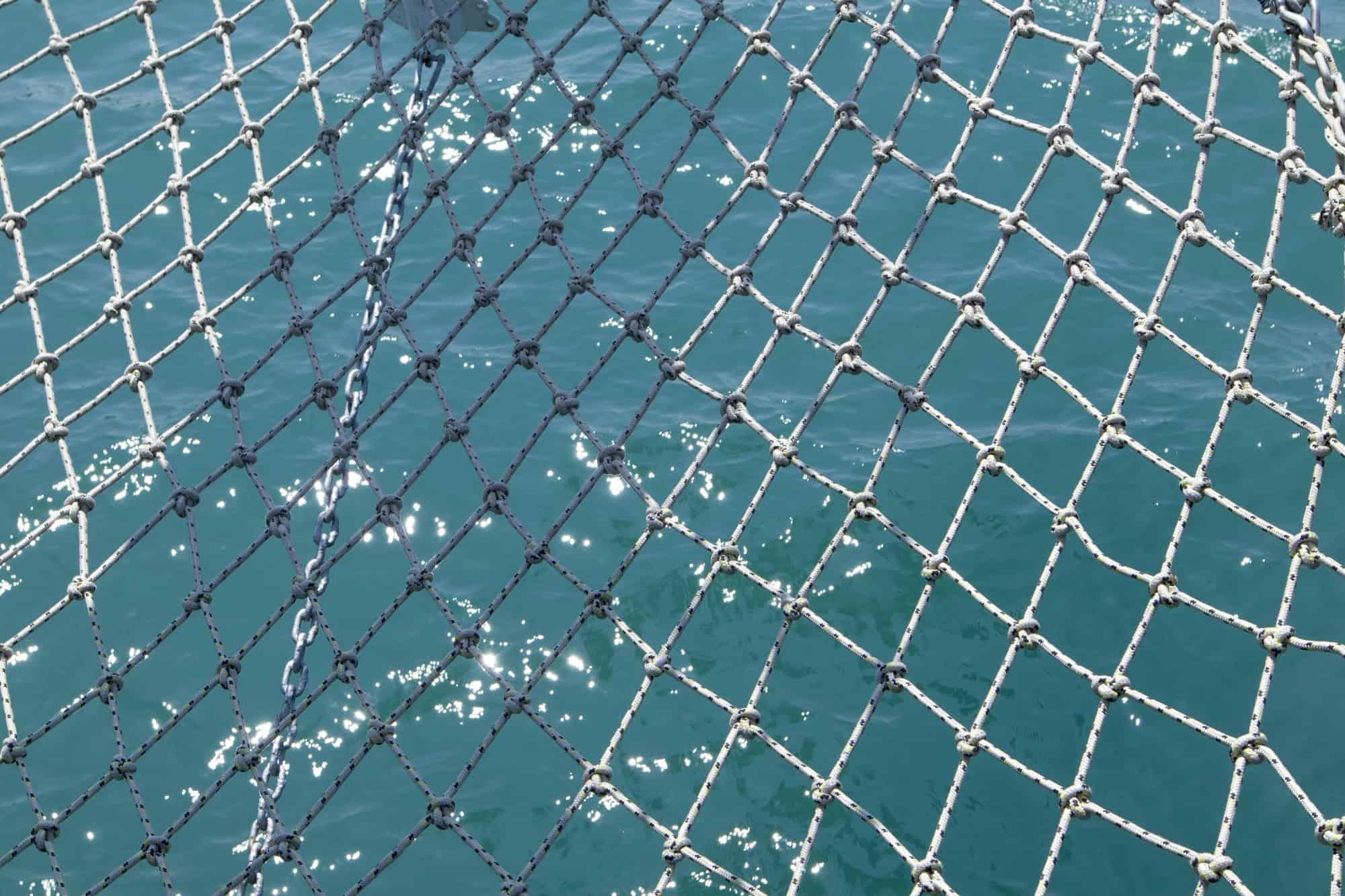 Close-up of a knotted fishing net stretched over turquoise water.