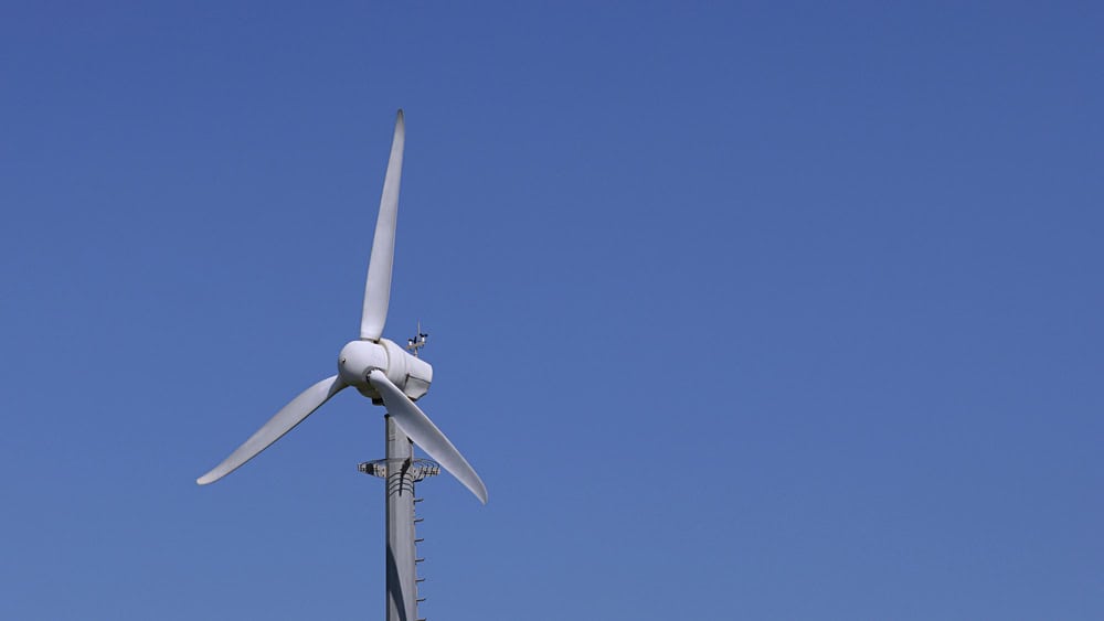 Wind turbine perched on a tall pole against a clear blue sky, illustrating renewable energy.