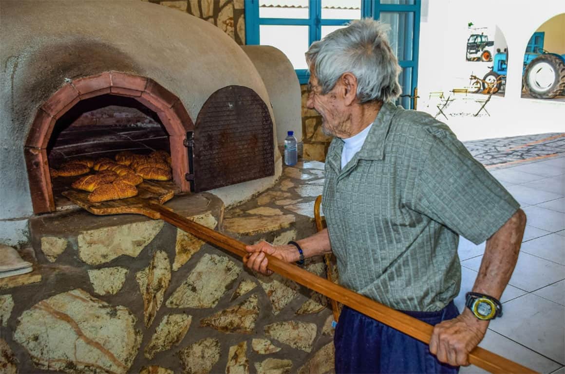 Male baker pulling bread out of a stone oven with a wooden baker's peel