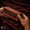 Black walnut eyewear case on dark fabric with gold glasses placed beside it