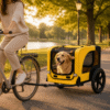 Dog enjoying a scenic ride in a yellow pet bike trailer attached to a bicycle, set in a golden-hour park environment with soft, natural lighting.